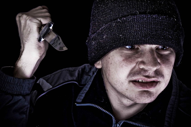 Young angry man with knife on black background